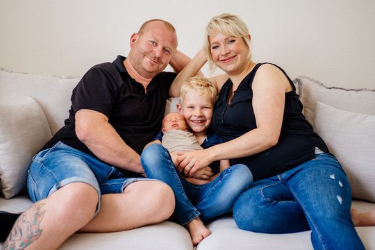 Vater Mutter großer Bruder und neugeborenes Baby kuscheln auf dem Sofa