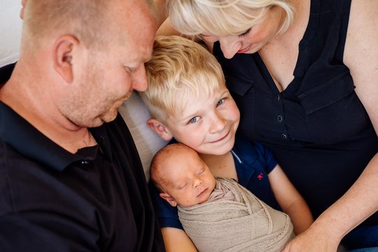 Vater Mutter großer Bruder und neugeborenes Baby kuscheln auf dem Sofa