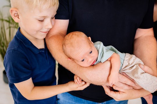 Großer Bruder lächelt Baby auf dem Arm vom Vater an