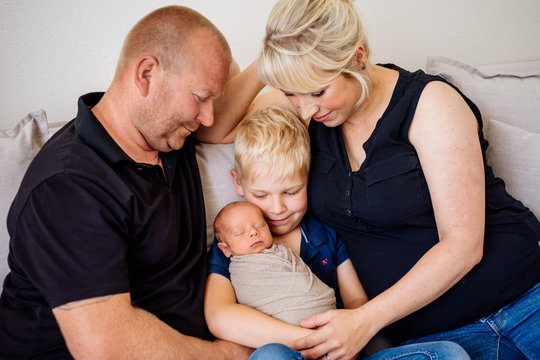 Vater Mutter großer Bruder und neugeborenes Baby kuscheln auf dem Sofa