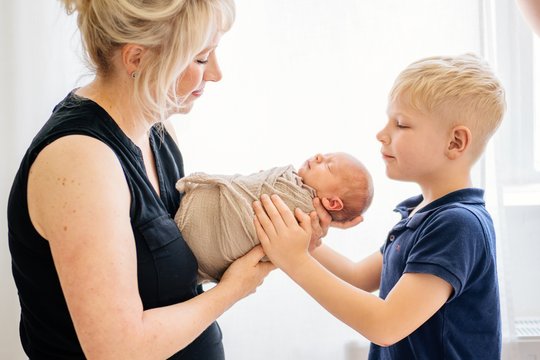 Mutter hält ihr Baby und großer Sohn schaut es an