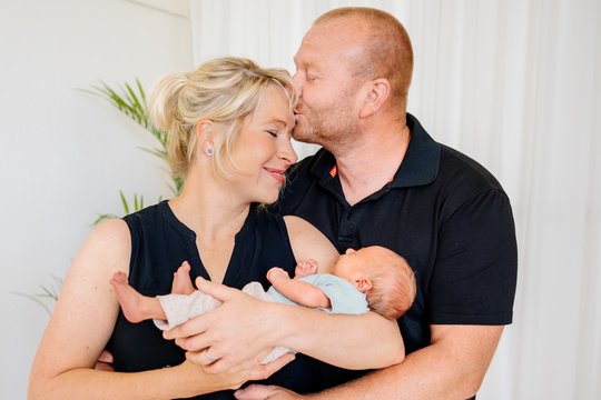 Mutter und Vater mit Baby auf dem Arm kuscheln