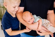 Großer Bruder lächelt Baby auf dem Arm vom Vater an